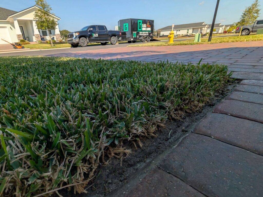 Freshly edged lawn along brick pavers with G&G Home Lawns truck and trailer in the background