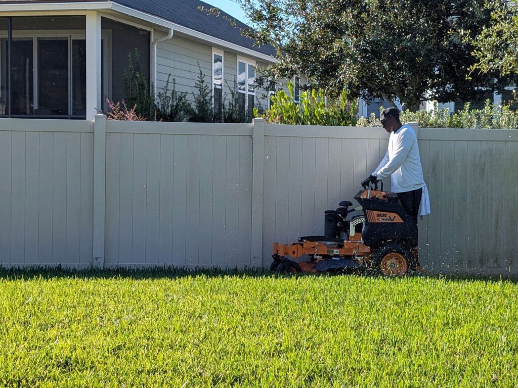 G&G Home Lawns team member performing residential lawn mowing along fence line in St. Johns County